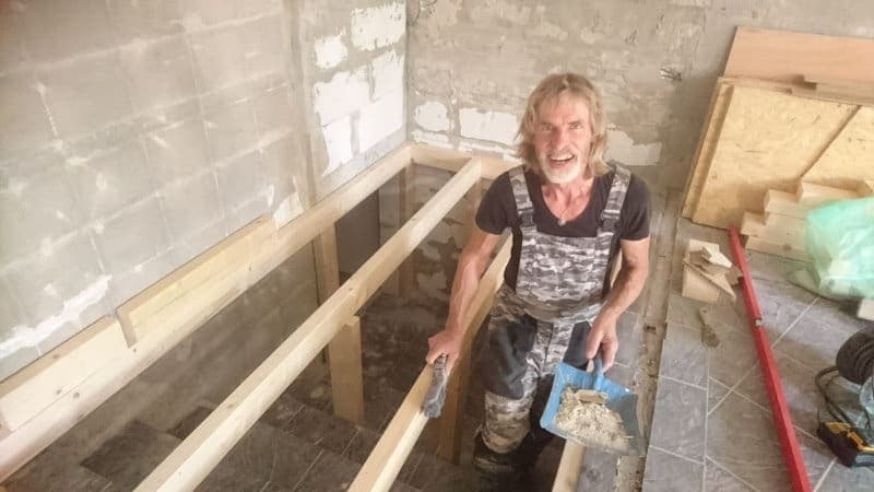 Michel met een troffel en een plak leem in zijn hand, lachend tijdens het werk aan een ruimte in opbouw